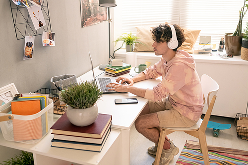 Contemporary teenager sitting by table in front of laptop in domestic room