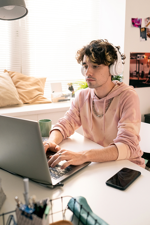 Contemporary guy with headphones looking at laptop display while typing