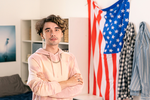 American teenager in casualwear crossing arms by chest against his bedroom