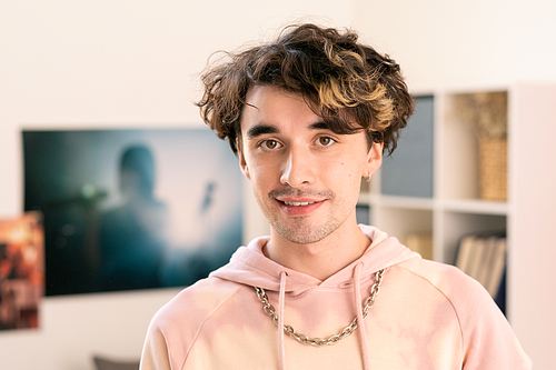 Contemporary teenager in pink hoodie looking at camera in home environment