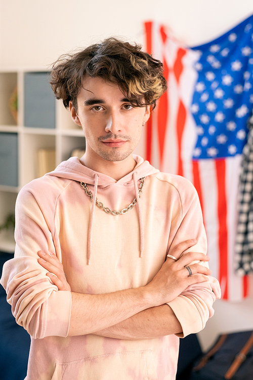 Youthful guy with his arms crossed by chest standing against American flag