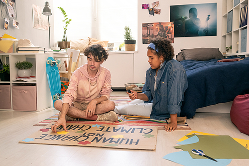 Two contemporary teenagers sitting on the floor and working over climate project