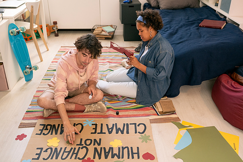 Male teenager with glue stick and his African girlfriend preparing climate project paper