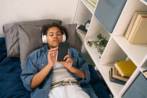 AFrican female teenager with headphones scrolling through playlist in smartphone