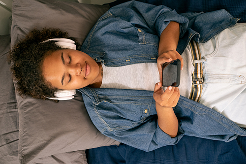 View of teenage girl listening to music in headphones while relaxing on bed