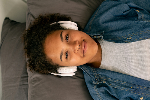 Cute teenage girl looking at you while listening to relaxation music in headphones