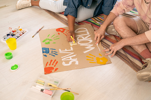 Contemporary teens sitting on the floor and drawing placard about saving world