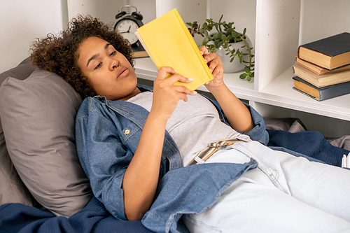 Pretty female student reading book before sleep while relaxing in bed