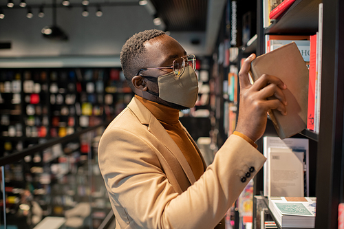 Young African man in smart casualwear choosing books in library or bookshop