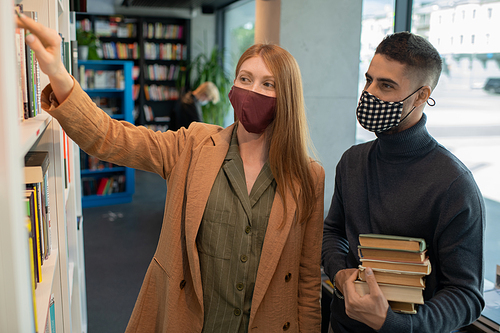 Two students or colleagues in protective masks choosing books in library or bookstore