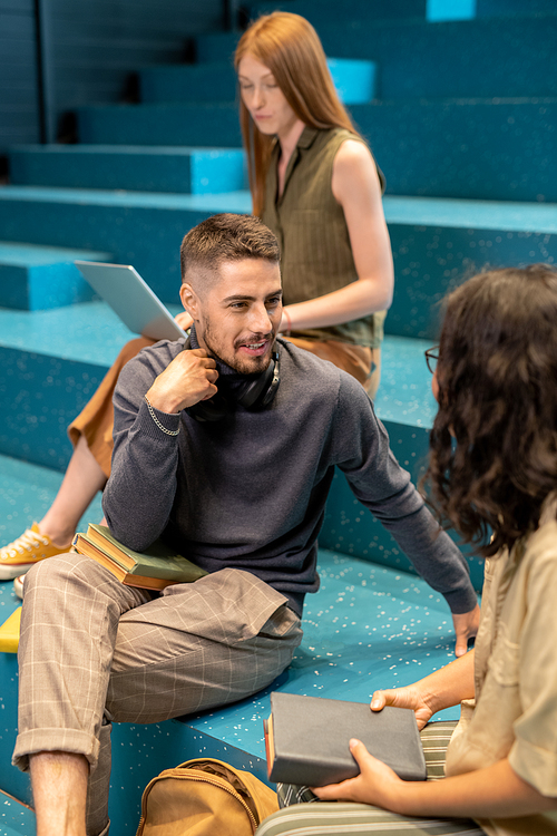 Contemporary businesspeople discussing working points while sitting on blue stairs against their colleague with laptop