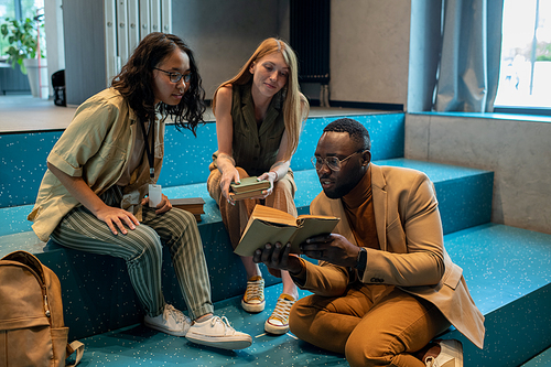 Young African man showing interest text in book to intercultural groupmates