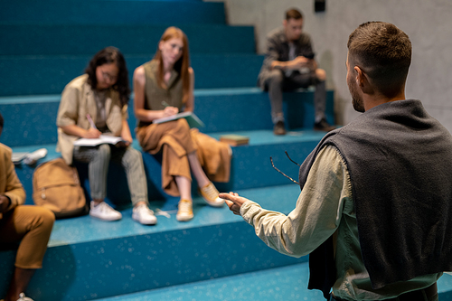 Rear view of young coach standing in front of audience during lecture or training