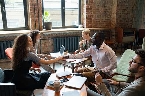 AFrican businessman shaking hand of young female colleague over workplace