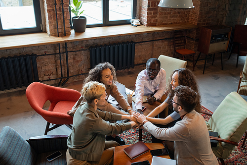 Several multiracial colleagues making pile of hands over workplace