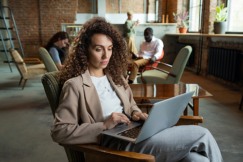 Young businesswoman using laptop while sitting in armchair in office