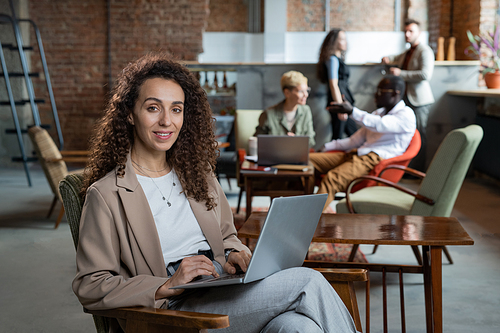 Happy young businesswoman with laptop sitting in armchair in working environment