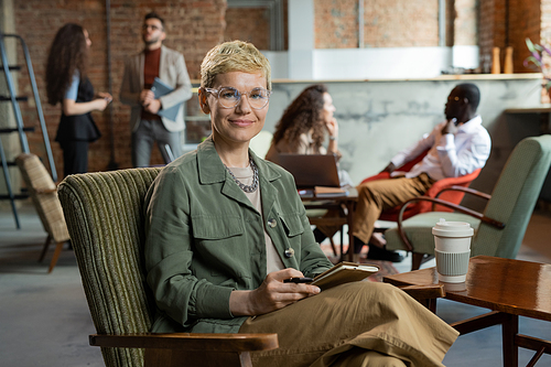 Young smiling businesswoman with short blond hair sitting in armchair