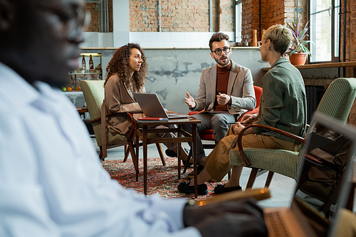 Three managers discussing their ideas by table in modern office or cafe