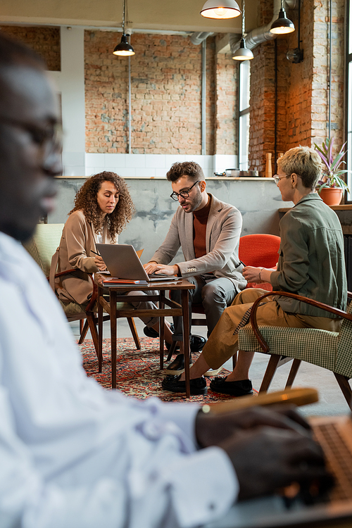 Young businessman computing by table among two female colleagues at meeting