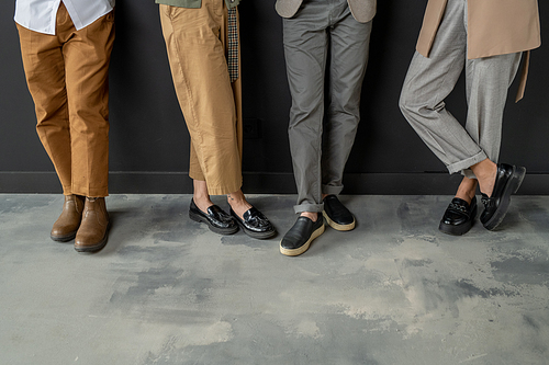 Low section of four businesspeople in smart casualwear standing along wall