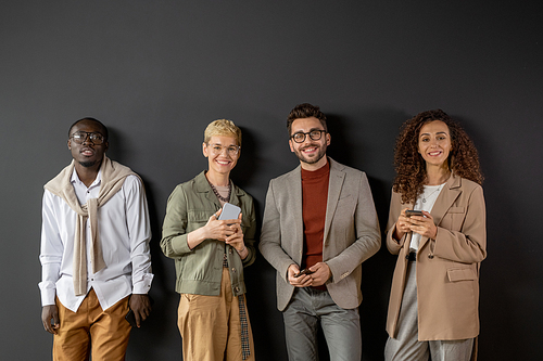 Young successful people with smartphones standing against grey wall