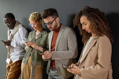 Row of young contemporary businesspeople scrolling in smartphones