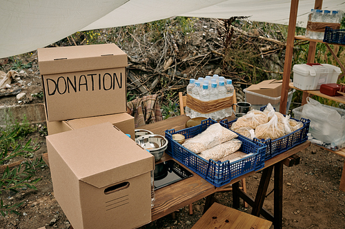Packed boxes with clothes and donation food on wooden table in large tent