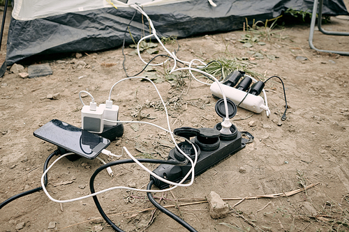 Smartphone and powerbanks charging on the ground by tent in refugee camp