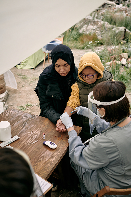 Female volunteer or doctor vaccinating little girl and her mother in refugee camp
