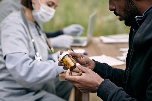 Young sick man from refugee camp holding bottle with pills prescribed him by doctor