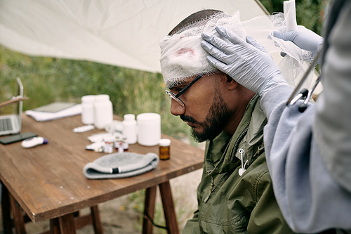 Unrecognizable nurse in gloves putting bandage on injured head of refugee in camp