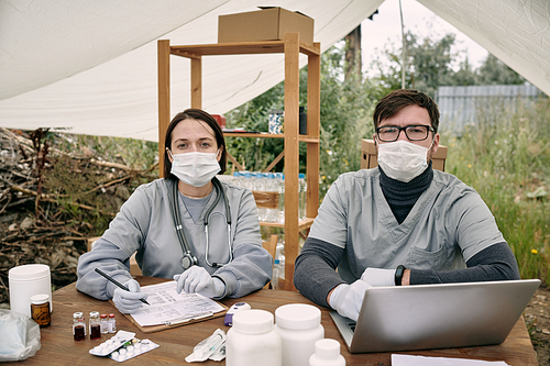 Two gloved clinician in uniform working by table in large tent in refugee camp
