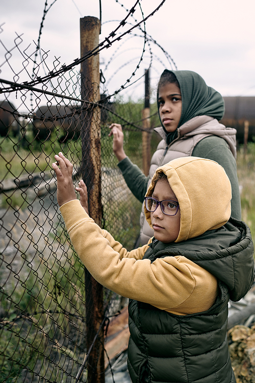 Sad lost middle eastern children standing at barbed wire and waiting for parents