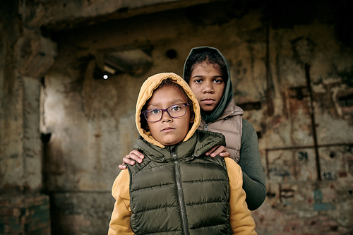 Portrait of two sisters in hoodies standing inside of abandoned house, they left alone after hostilities