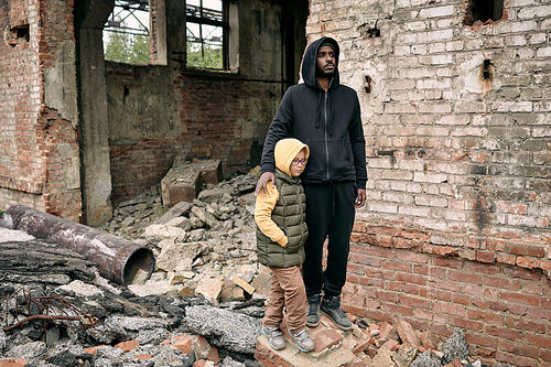Young man and little girl standing by abandoned ruined building against brick wall