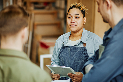 Warm toned portrait of female artisan consulting clients in carpentry workshop