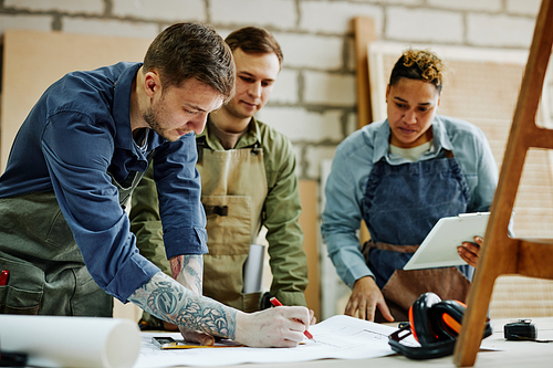 Warm toned portrait of modern artisans discussing furniture designs in carpentry workshop