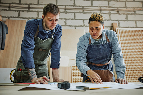 Low angle portrait of two artisans discussing furniture designs in carpentry workshop