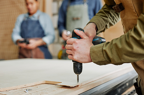 Close up of male carpenter drilling wood while building handmade furniture in workshop, copy space