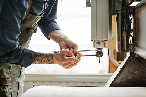 Side view closeup of tattooed worker repairing machine units in workshop, copy space