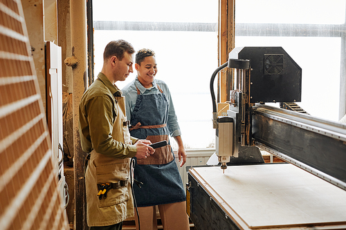 Side view portrait of two carpenters operating CNC laser machine in automated woodworking production