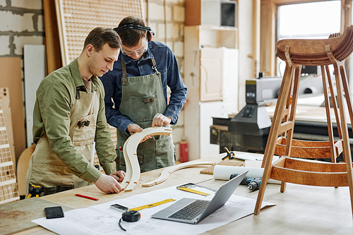 Warm toned portrait of two workers fitting wood parts while building handcrafted furniture in workshop, copy space