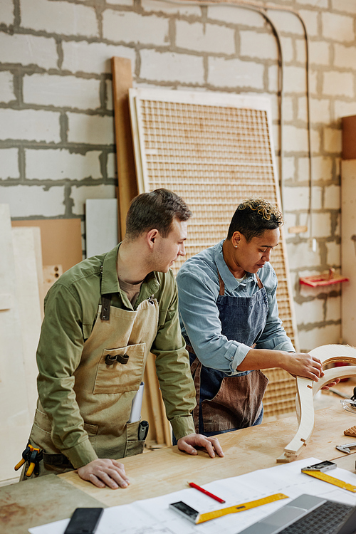 Vertical portrait of two carpenters designing handcrafted furniture piece in workshop