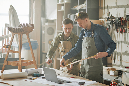 Portrait of two male carpenters building handcrafted wooden furniture in hazy workshop, copy space