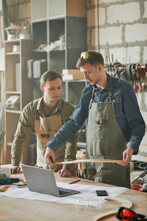 Vertical shot of two male carpenters designing handcrafted furniture in hazy workshop