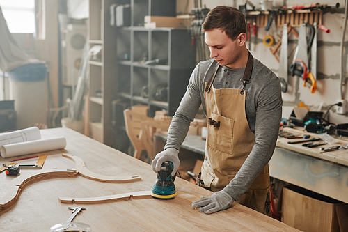 Portrait of young carpenter sanding piece of handcrafted wooden furniture in hazy workshop, copy space