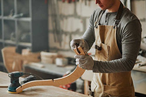 Moody closeup of young carpenter sanding wood while building handcrafted furniture in workshop, copy space