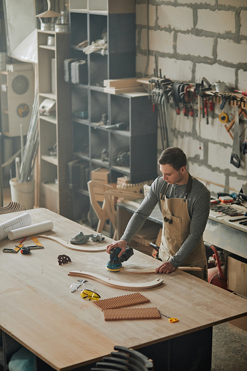 Mood shot of young carpenter working alone in shop and sanding piece of handcrafted furniture