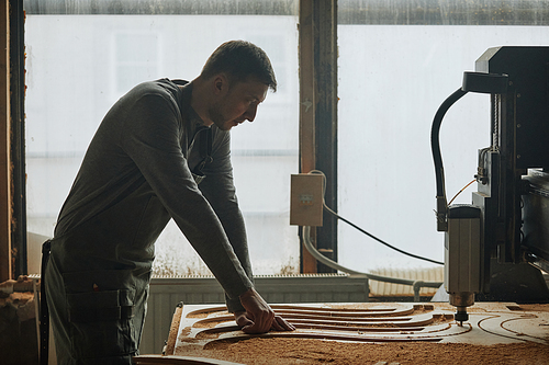 Silhouette shot of male carpenter cutting wood by window in workshop, copy space